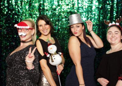 Women posing with holiday props in front of a green sequin backdrop.