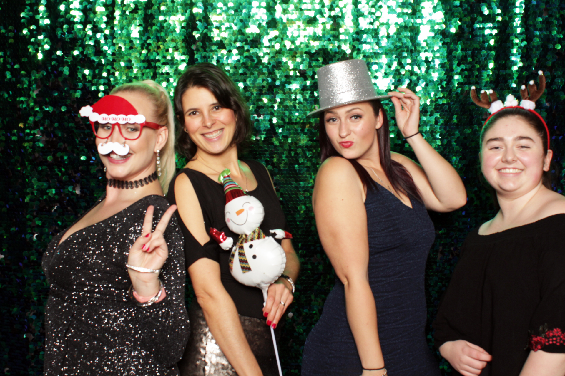 Women posing with holiday props in front of a green sequin backdrop.